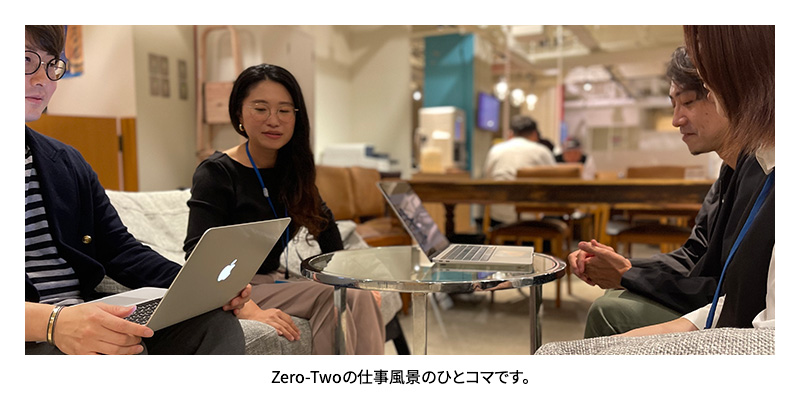 スタッフ4名がテーブルを囲み、打ち合わせをしている写真に加え、その下側にテキストで「Zero-Twoの仕事風景のひとコマです。」と表示された画像。